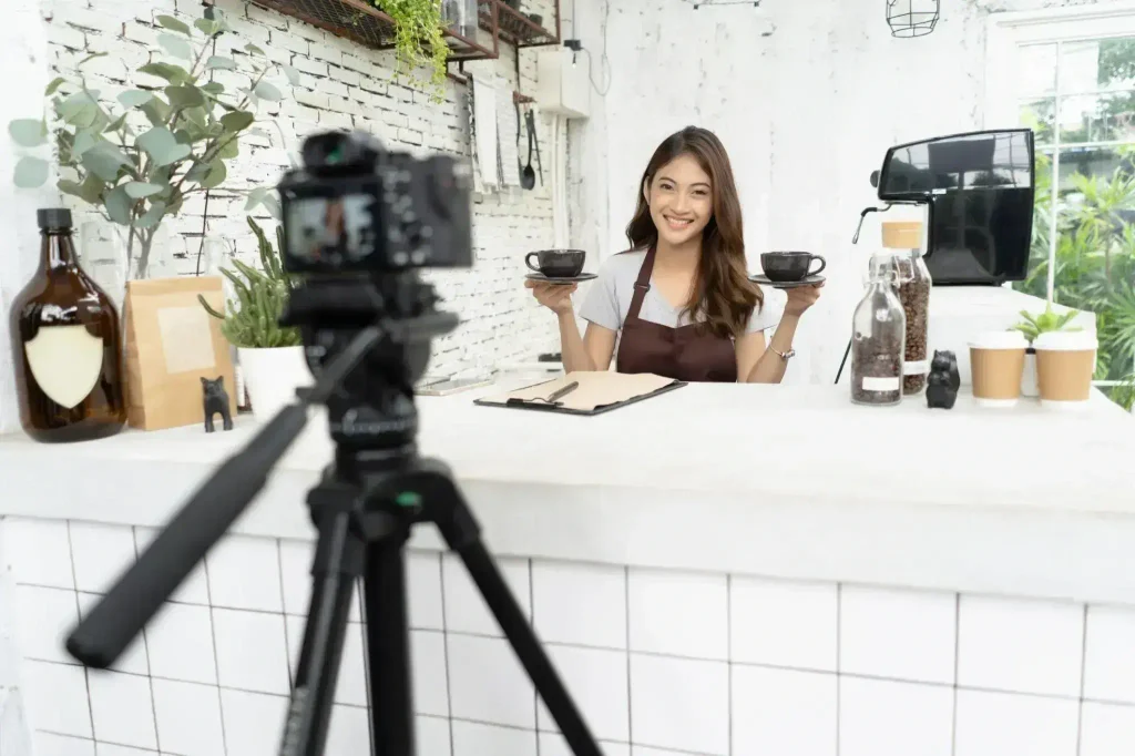 Woman holding two cups in front of a camera while creating content for customers